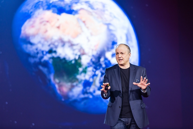 Pellegrino Riccardi giving a talk with an image of the Earth seen from space in the background