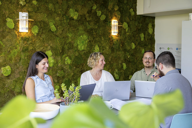 Four UiO employees sit around a meeting table. Moss wall in the background.