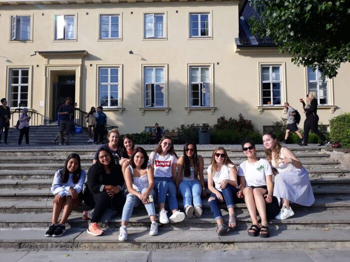 Students sitting on steps of Blindern Studenterhjem in front of main building - building is faded light yellow