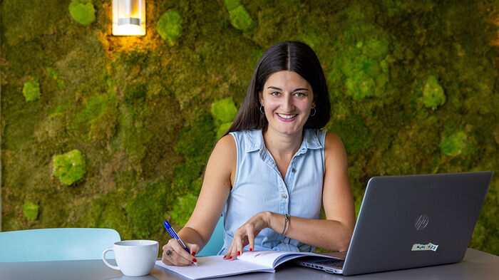 Person sitting at a desk with laptop in front of a green wall