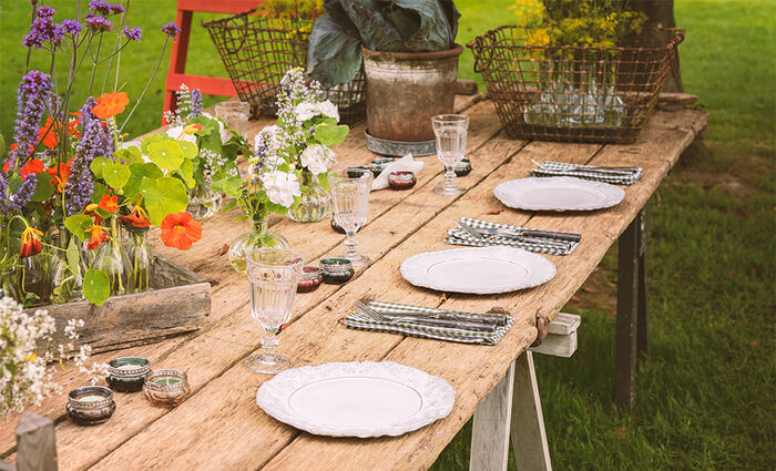 Trebord på en gressplen dekket med hvitt servise og blomster på bordet.