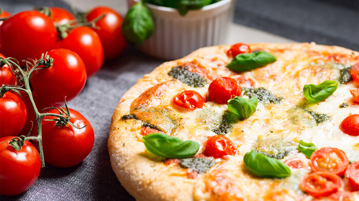 Pizza på et bord med en klase tomater til venstre.