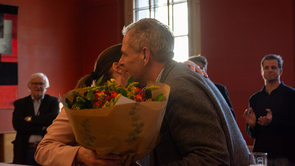 Kvinne og mann klemmer under overrekkelse av blomster.