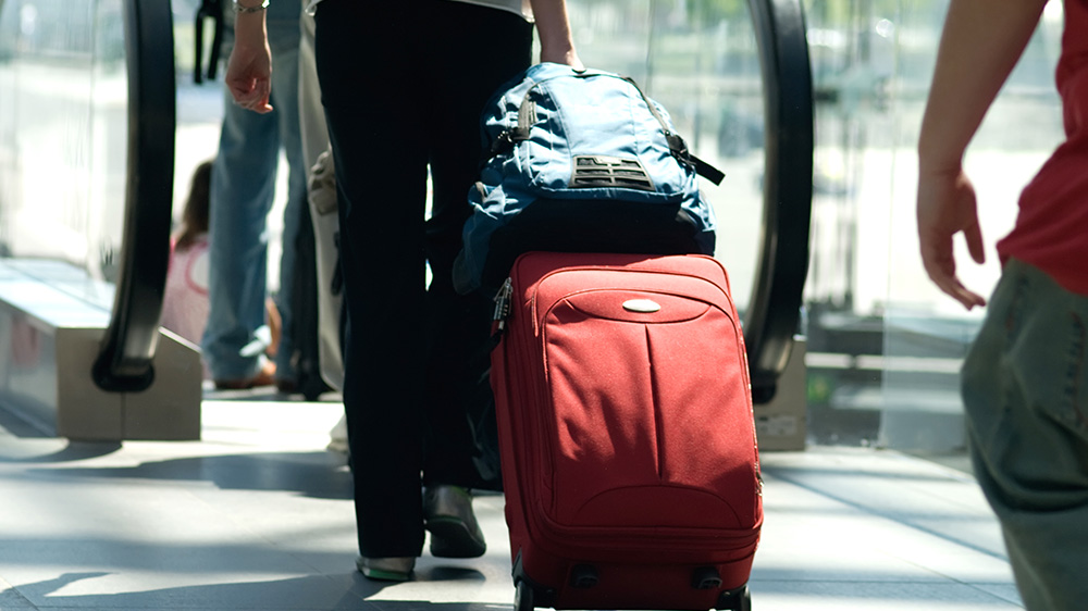 Person triller rød koffert med ryggsekk til rulletrapp.