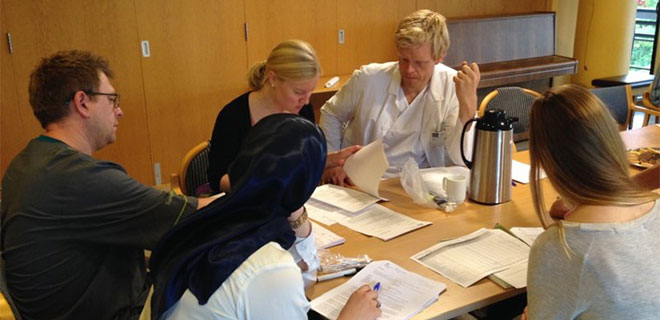 Fem personer i diskusjon rundt et bord med papirer