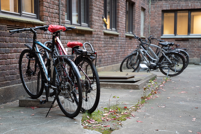 Image of bicycles parked in a bicycle rack next to a brick wall with windows