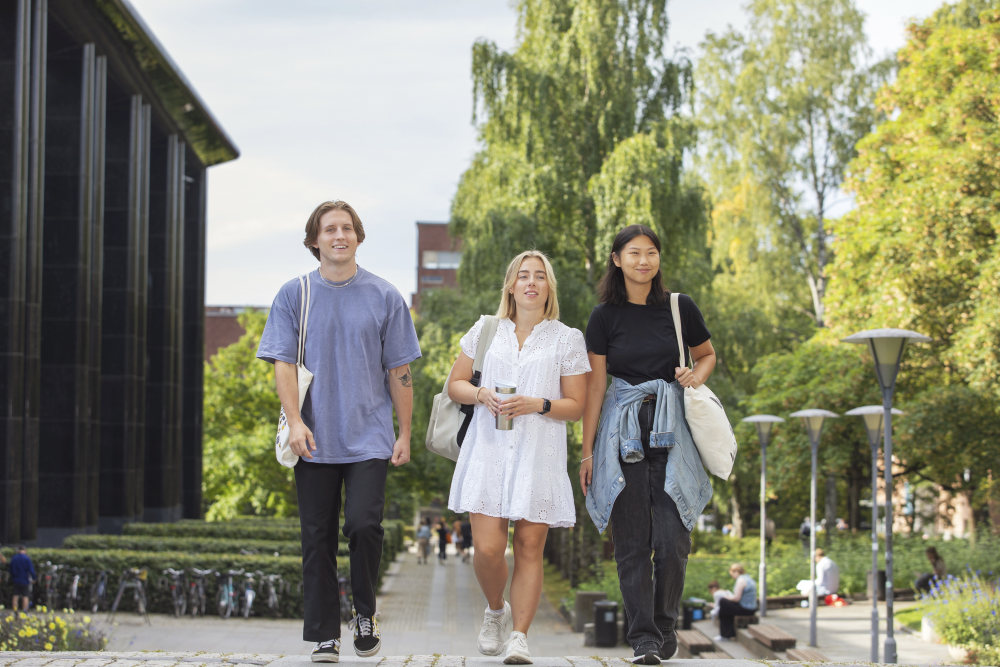 smilende studenter som spaserer, med campus i bakgrunn og grønne omgivelser rundt seg