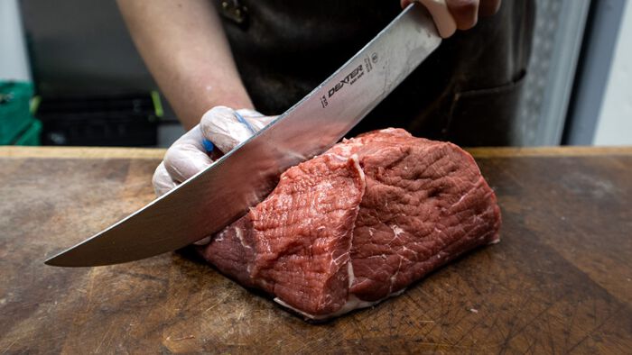 Et kjøttstykke som blir kuttet opp av en stor kniv. 