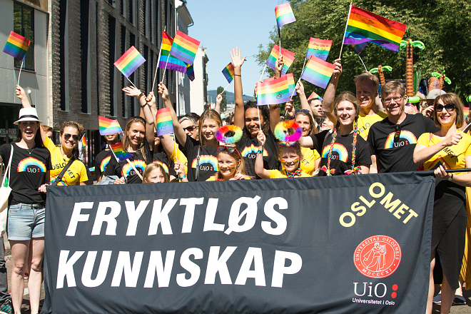 Studenter og ansatte fra UiO og OsloMet i Pride-T-skjorter vifter med Pride-flagg og holder opp banneret "Fryktløs kunnskap"