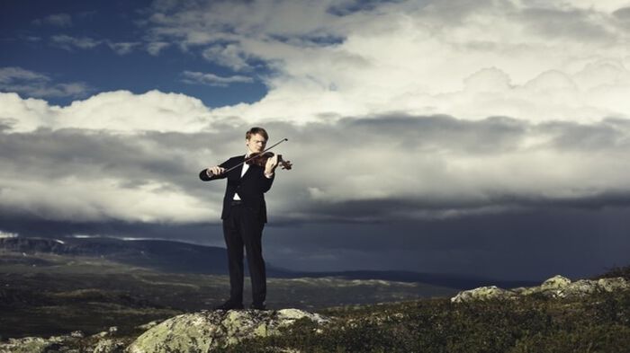 Mann på fjelltopp som spiller fiolin