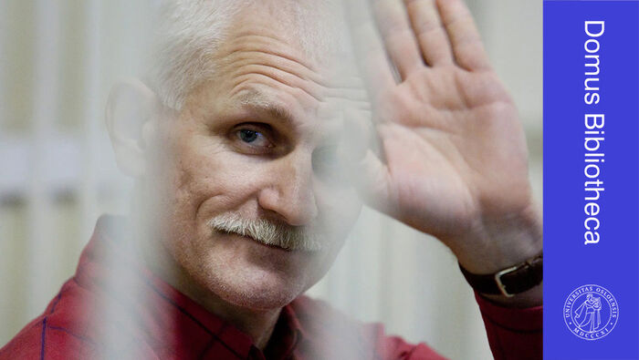 Ansikt og hånd til Ales Bjaljatski bak grått fengselsgitter