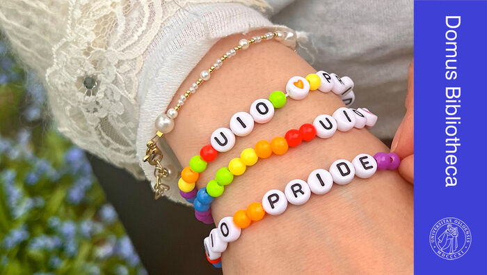 Nærbilde av hånd med perlearmbånd i ulike farger og bokstavperler med "UiO" og "Pride"