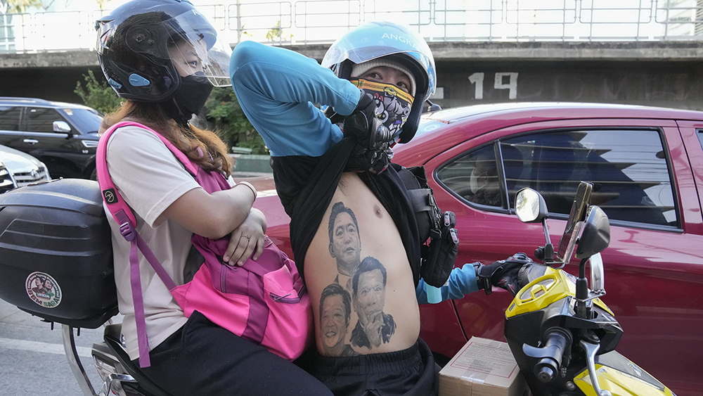 En kvinne og en mann på moped. Mannen viser tre tatoveringer på overkroppen, av presidentene Bong Bong Marcos, Rodrigo Duterte og Ferdinand Marcos.