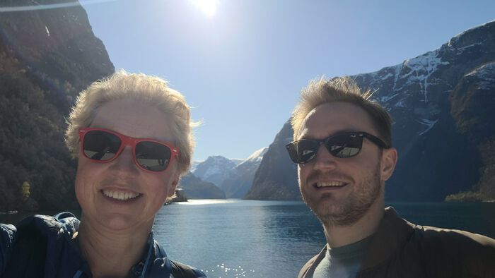 Caroline Palmer and Valentin Bégel in the foreground, a Norwegian fjord with snowy mountains and sunshine in the background.
