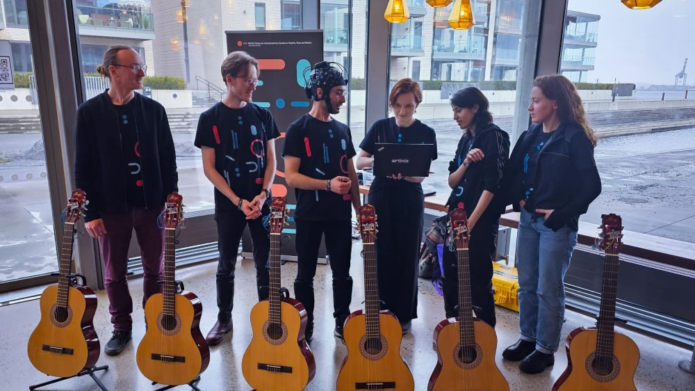 Six persons standing behind six guitars