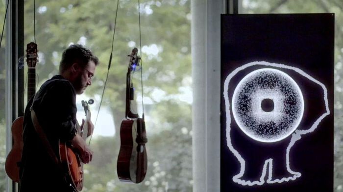 Çağrı Erdem playing guitar in front of two suspended guitars