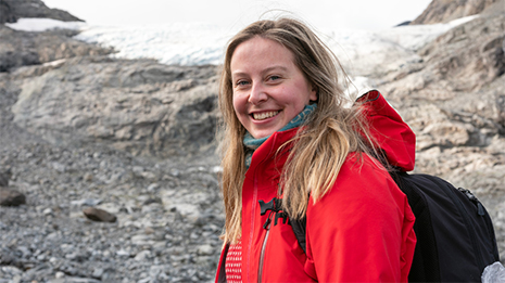 Kvinnelig student smiler mot kamera i turklær foran et snøkledd fjell