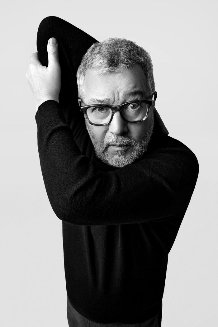 Bilde av Philippe Starck. Han har på seg en svart genser og svarte briller. Han gjør en grimase og holder en arm bak skulderen