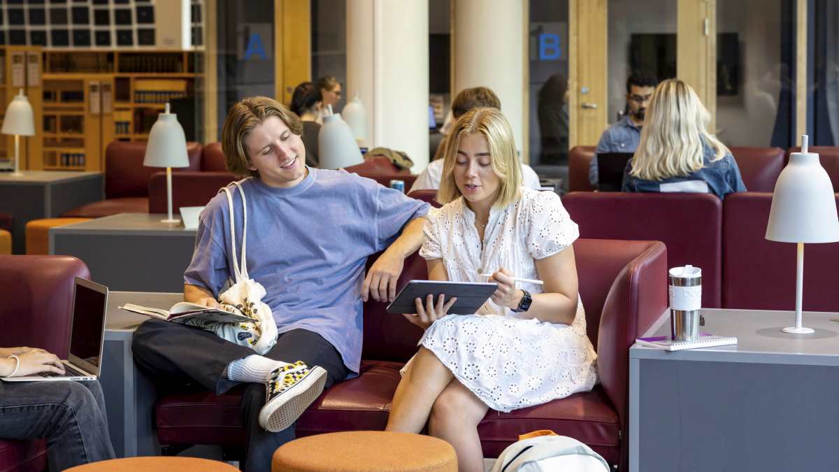 Mann- og kvinnelig student i sofa som ser på felles iPad
