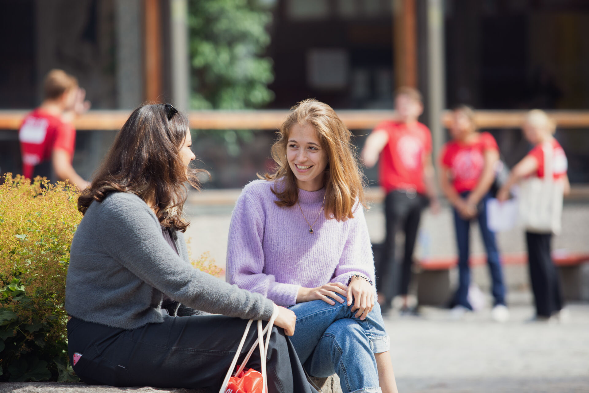 To kvinnelige studenter smiler og prater på en benk ute
