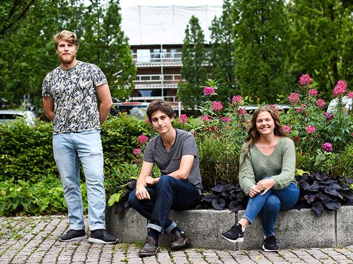 tre studenter foran et sommergrønt og blomstrende campus