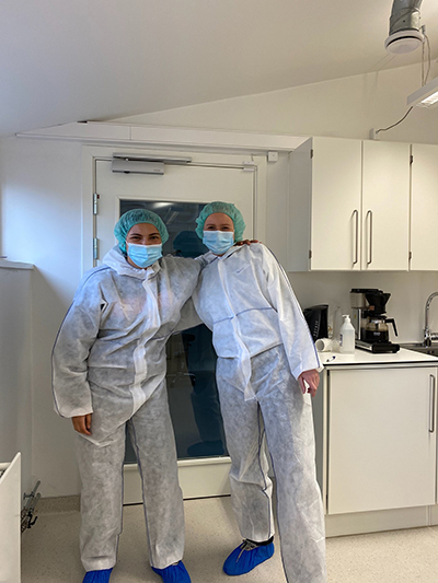 To kvinner i laboratoriet iført beskyttelsesutstyr og munnbind