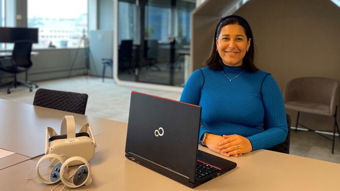 Bildet viser en kvinne som sitter ved et bord med VR-briller og PC