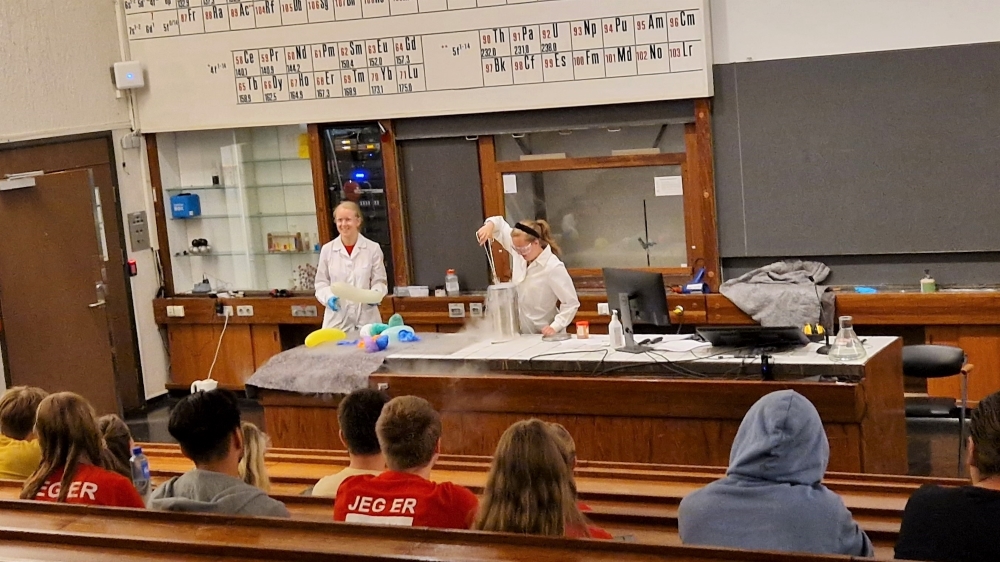 Mathilde og Veronica utfører kjemiske eksperimenter forann faddere og fadderbarn i et auditorium.