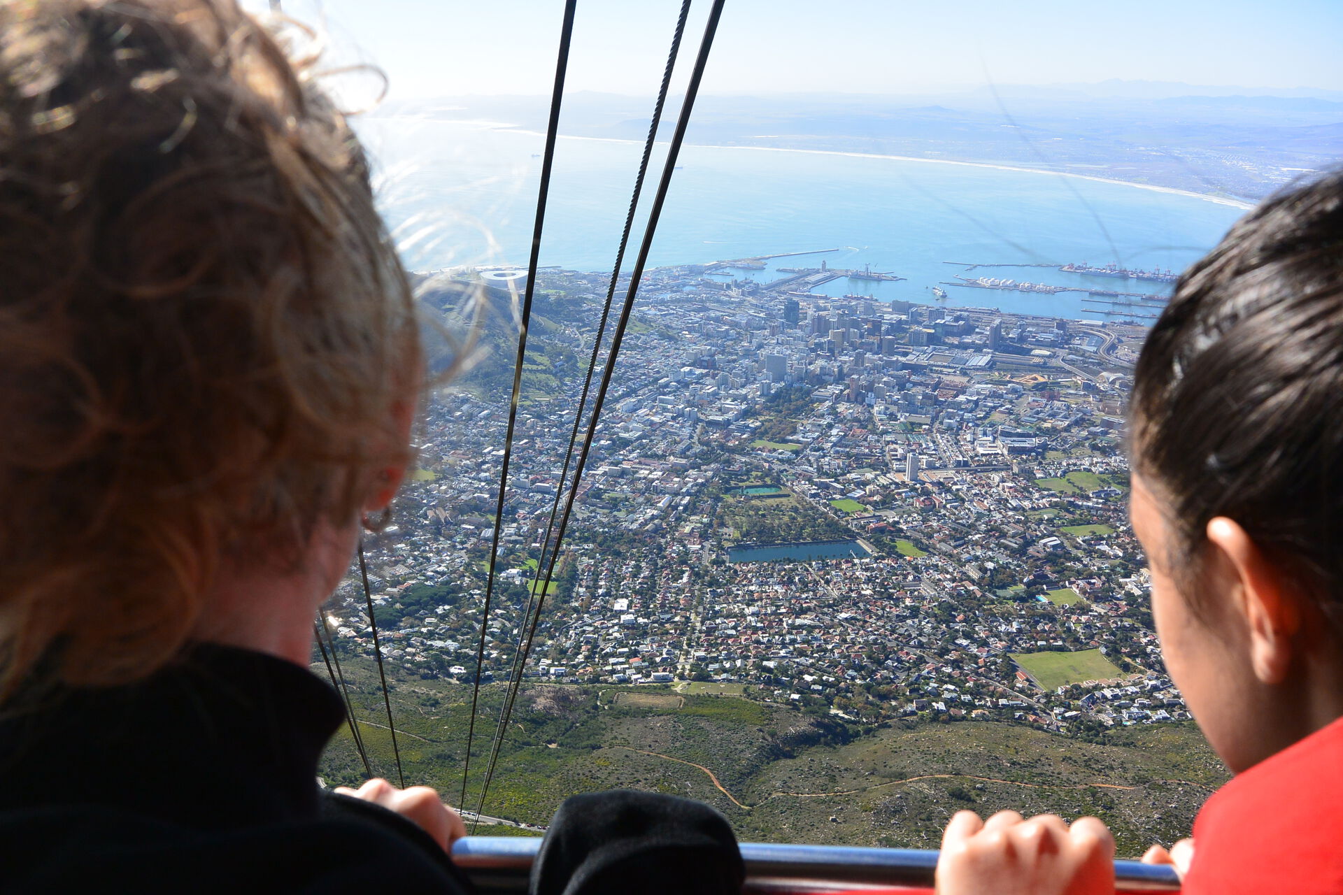 Bakhodet til to personer som kjører en gondol opp et fjell og ser ned på byen Cape Town
