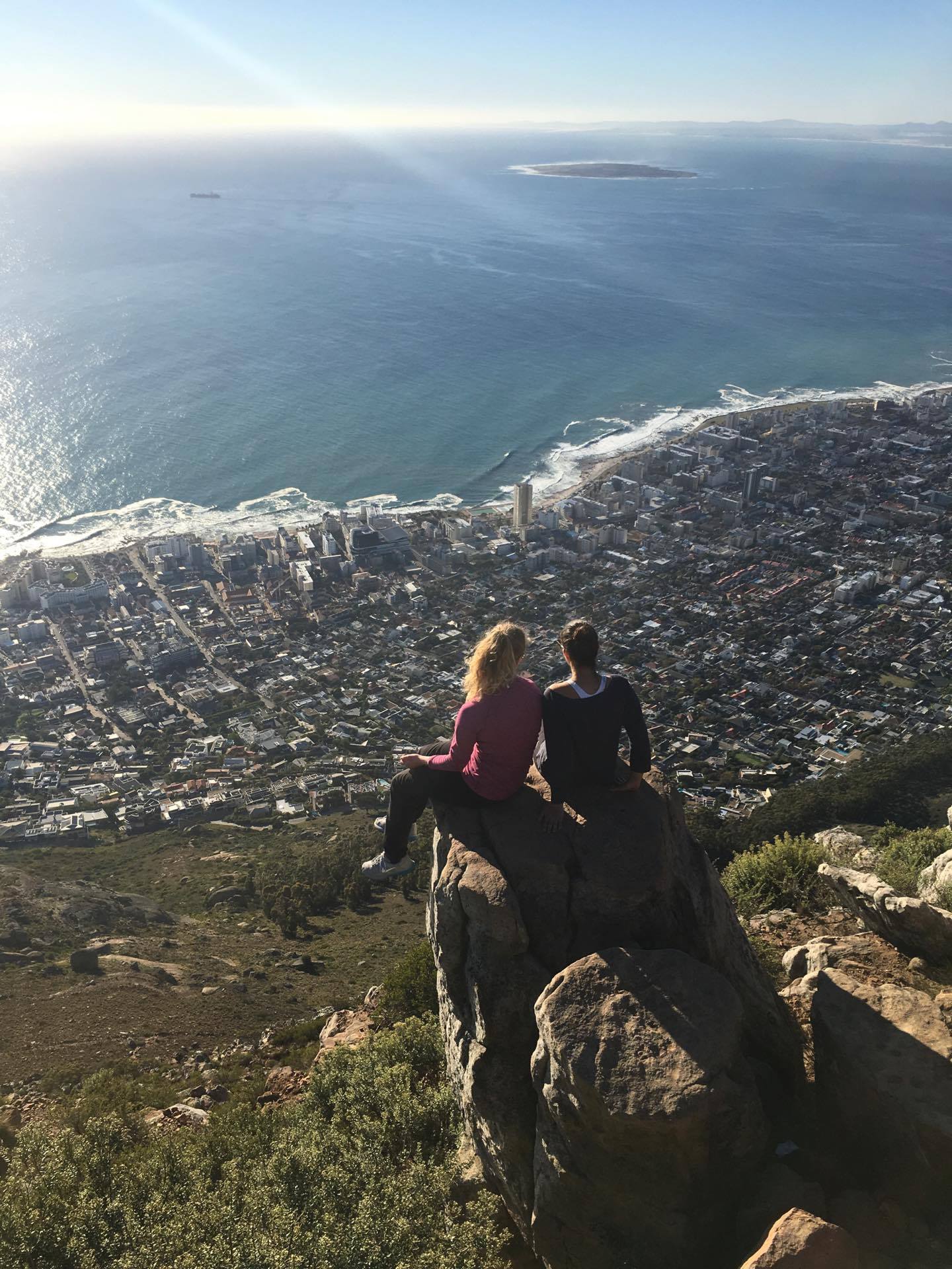To personer som sitter på tuppen av Table Mountain (et fjell i Cape Town) og titter utover byen som er i bakgrunnen