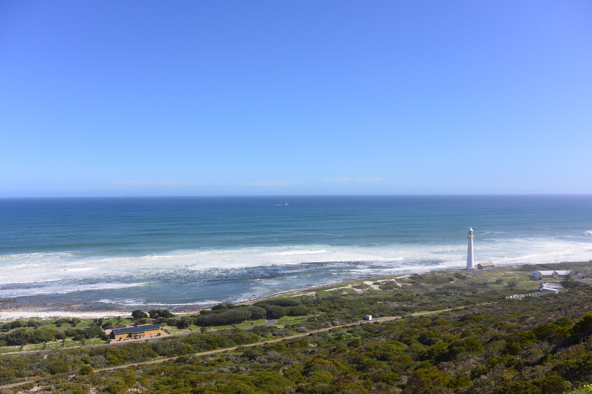 Utsikt over et grønt område som møter havet med et fyrtårn i strandkanten