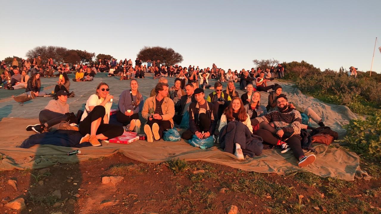 Studenter sitter i solnedgangen på et fjell i Cape Town