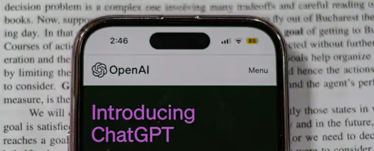 Bilde av mobiltelefon som ligger oppå en bok og åpningsskjermen til ChatGPT er på mobilen